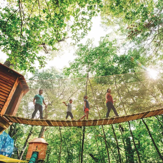 A group of individuals crossing a suspension bridge in a serene woodland setting.