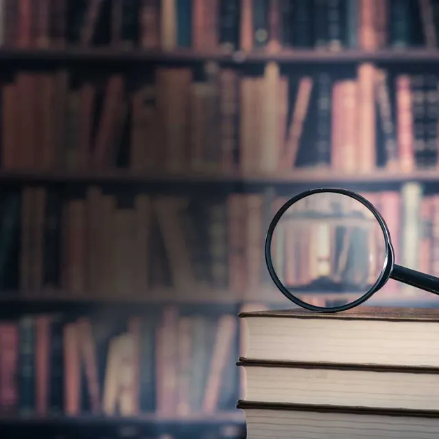 A magnifying glass resting on a wooden bookshelf filled with various books.