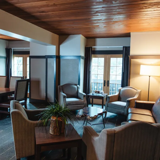 Cozy lounge area featuring two armchairs, a leather sofa, a wooden dining table, and large windows with natural light.