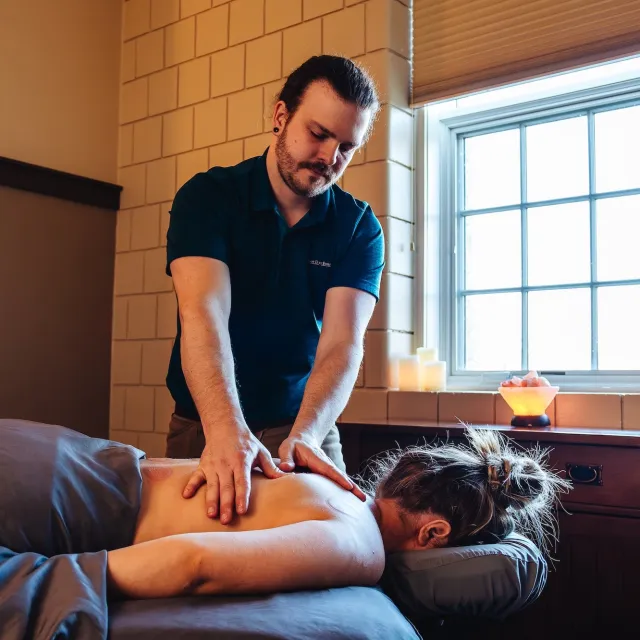 A person receiving a massage in a serene spa setting, with candles and a window offering natural light in the background.