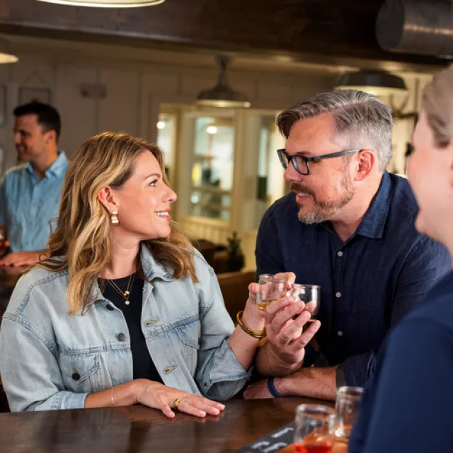 A lively bar scene with two people engaged in conversation, holding drinks; others socialize in the background.