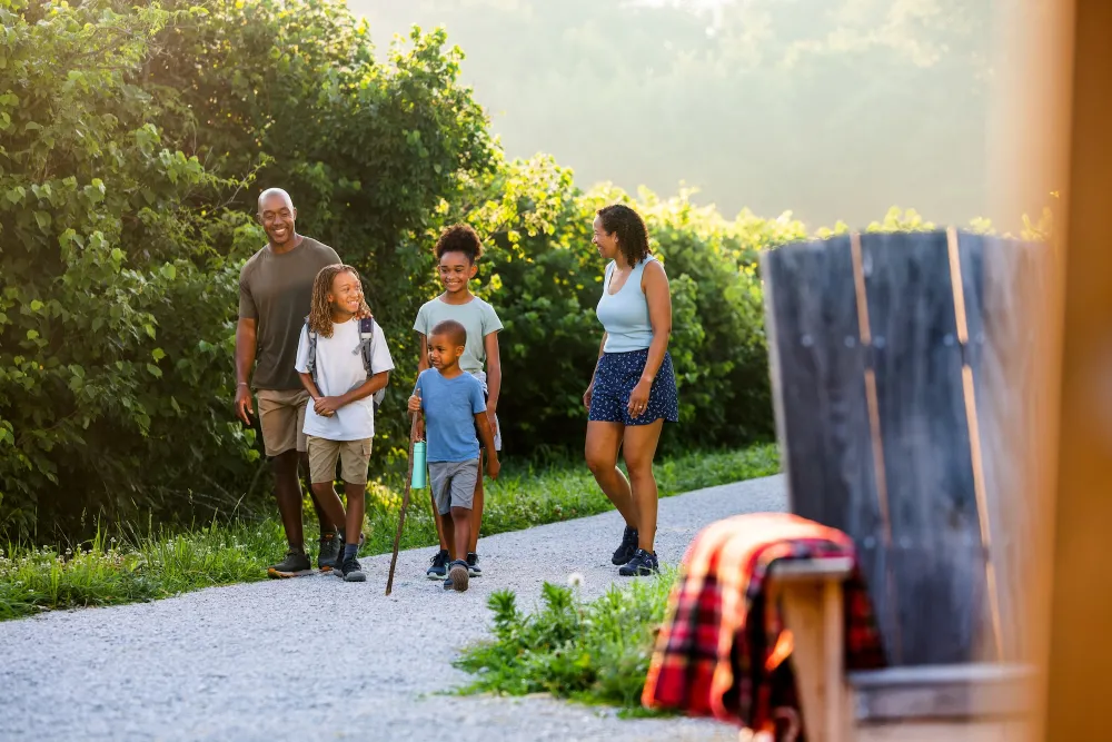 A family of five walks along a gravel path surrounded by lush greenery, enjoying a sunny day outdoors.