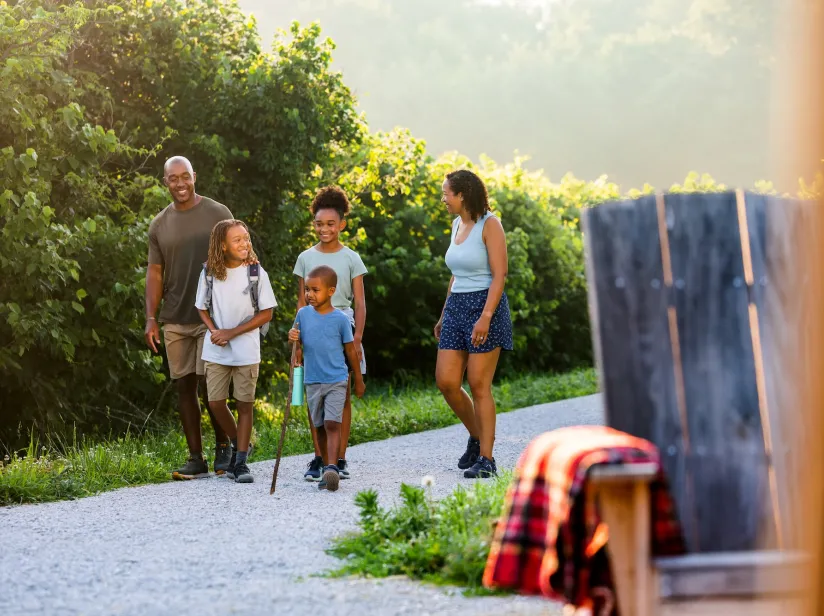 A family of five walks along a gravel path surrounded by lush greenery, enjoying a sunny day outdoors.