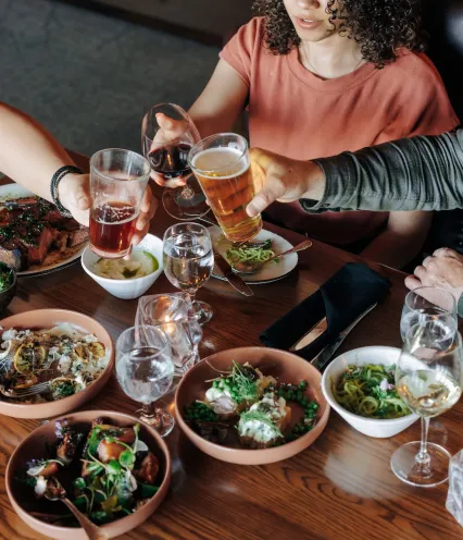 A table filled with various dishes and drinks, as friends raise their glasses for a toast during a lively dining experience.
