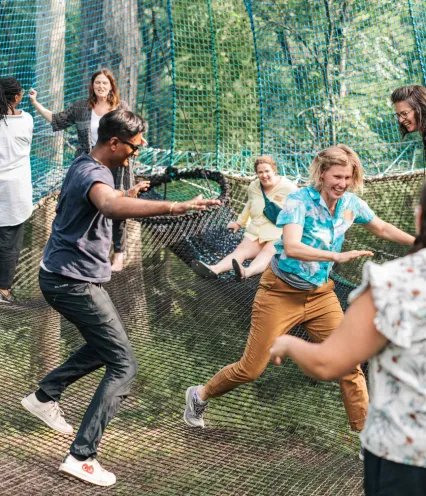 A group of people joyfully playing on a large net trampoline surrounded by lush greenery, capturing a lively moment of fun.