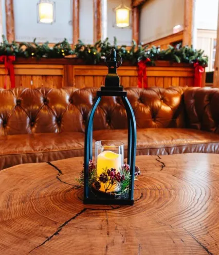 A cozy lounge with a brown leather sofa, a rustic wooden coffee table, and a lantern centerpiece featuring a lit candle and greenery.