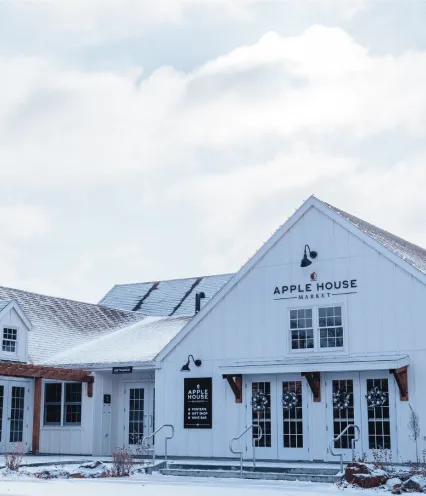 Exterior view of the Apple House Market, a modern white barn-style building with snow on the roof and ground.