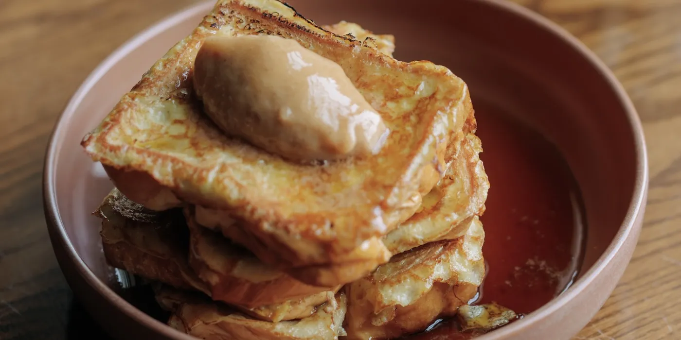 Stack of golden French toast with a dollop of creamy butter on top, served in a deep plate with a drizzle of syrup.