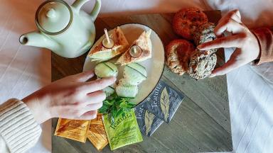 A person presenting a tray filled with an assortment of food and a cup of tea.