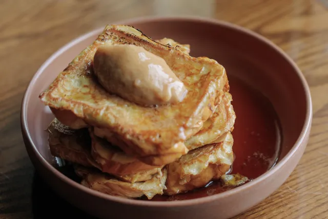 Stack of golden French toast with a dollop of creamy butter on top, served in a deep plate with a drizzle of syrup.
