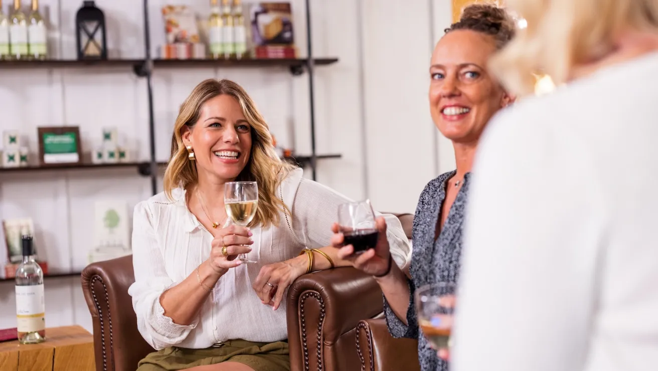 Two women relax on a couch, each holding a wine glass, enjoying a cozy moment together.