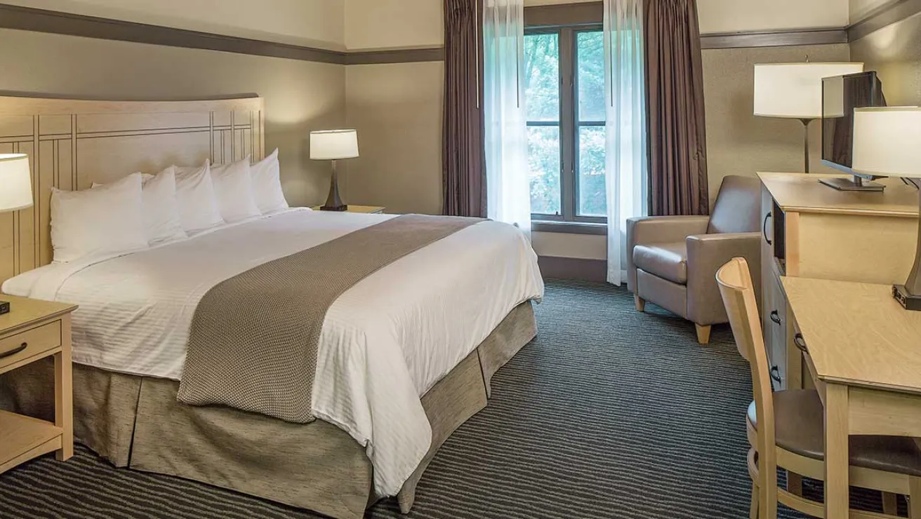 A hotel room featuring a neatly made bed, a desk with a chair, and warm lighting creating a cozy atmosphere.