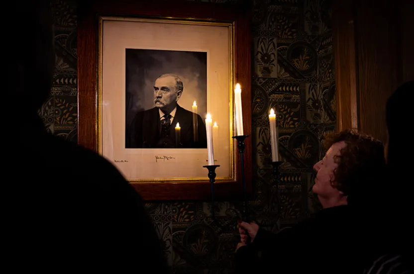 Woman holding candlestick looking at portrait on the wall in the dark.