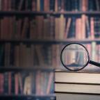 A magnifying glass resting on a wooden bookshelf filled with various books.