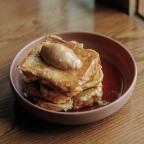 Stack of golden French toast with a dollop of creamy butter on top, served in a deep plate with a drizzle of syrup.